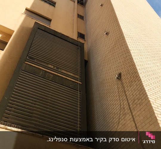 אדם עובד בגובה על בניין עם חבלים וכלים